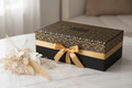 Matte black rigid gift box with gold ribbon on white marble